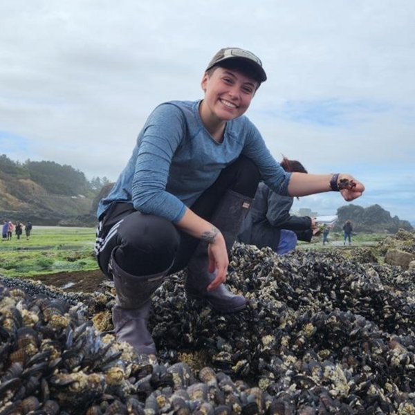 Tandi Venema crouches atop a bed of mussels holding a crab